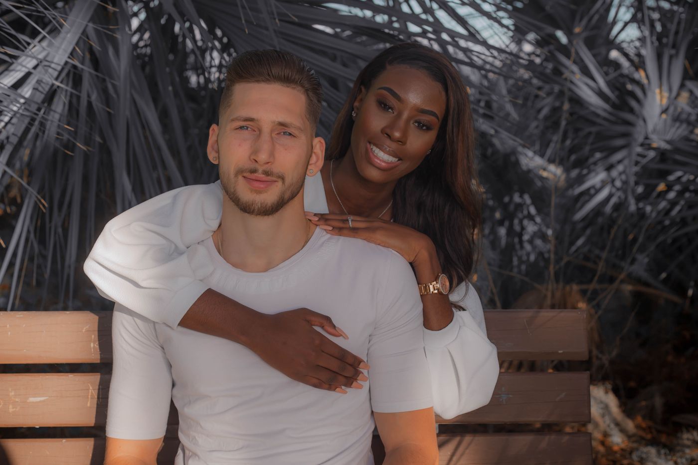 A white man and a black woman sitting together on a bench, both smiling.